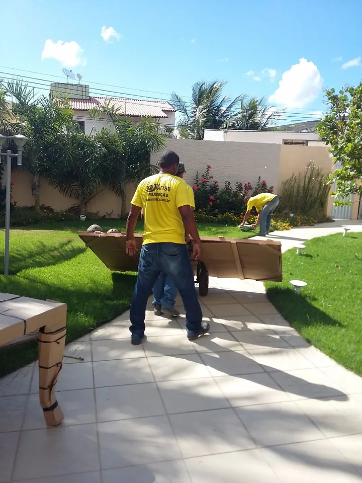 Equipe da Arise carregando móveis embalados no jardim de uma residência em Maceió
